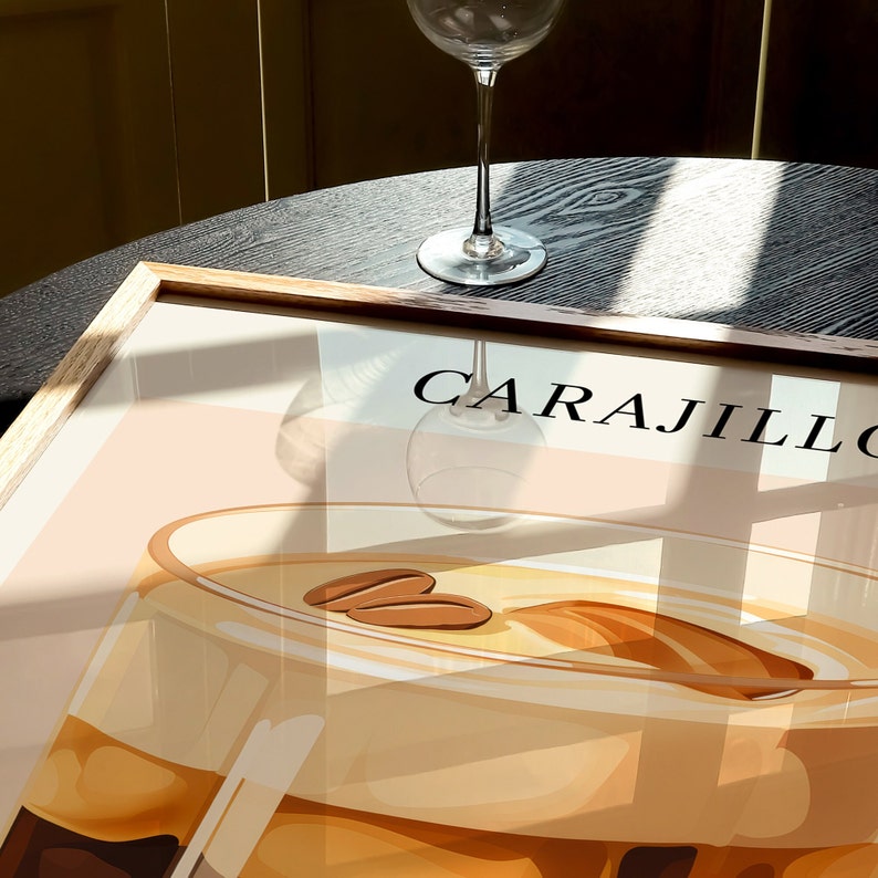 May include: A framed illustration of a glass of Carajillo, a Spanish coffee cocktail. The drink is a light brown color with coffee beans floating on top. The text "CARAJILLO" is printed in white on a light pink background.