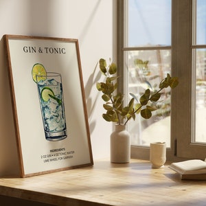 May include: A framed illustration of a Gin & Tonic cocktail recipe. The illustration shows a glass filled with gin, tonic water, and ice, garnished with a lime wheel. The text reads "Gin & Tonic" and "Ingredients: 2 oz Gin + 4 oz Tonic Water, Lime Wheel for Garnish".