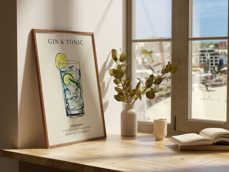 May include: A framed illustration of a Gin & Tonic cocktail recipe. The illustration shows a glass filled with gin, tonic water, and ice, garnished with a lime wheel. The text reads "Gin & Tonic" and "Ingredients: 2 oz Gin + 4 oz Tonic Water, Lime Wheel for Garnish".