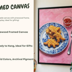 K&ouml;nnte beinhalten: Gerahmtes Leinwandbild mit einem Stillleben aus Dinosaurier-Nuggets auf einem blau-wei&szlig;en Teller, mit Ketchup und einer Gabel. Der Hintergrund ist rosa. Die Leinwand ist schwarz gerahmt.
