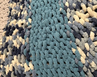 Könnte beinhalten: Eine dicke Strickdecke in Blau, Weiß und Grau. Die Decke ist aus dickem Garn gefertigt und hat eine weiche, flauschige Textur.
