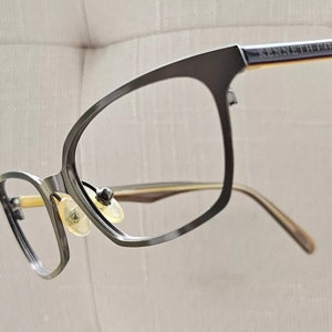 May include: Black eyeglasses with a gold metal frame and the text "KENNETH COLE" on the side.