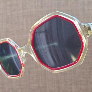 May include: Clear plastic sunglasses with red trim and octagonal lenses.