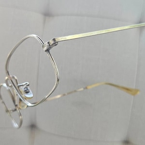 May include: Silver-toned eyeglasses with a unique, curved frame design. The glasses feature a square lens shape and slender temples. The overall aesthetic is minimalist and modern, suitable for everyday wear.