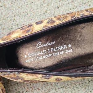 May include: Close-up of a shoe interior with a leopard print exterior. The shoe's insole is brown with the text "Couture DONALD J PLINER MADE IN THE MOUNTAINS OF ITALY". The shoe has a dark brown trim.