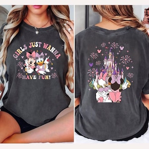 May include: Dark grey t-shirt featuring Minnie Mouse and Daisy Duck with the text "GIRLS JUST WANNA HAVE FUN!" on the front. The back of the shirt shows a castle with fireworks and the same characters. The shirt is a comfortable, casual style.