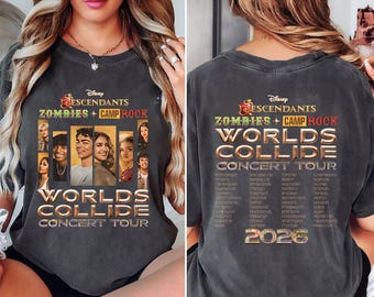 May include: A dark gray t-shirt featuring the text "Descendants Zombies + Camp Rock Worlds Collide Concert Tour" with a graphic of the cast. The back of the shirt also has the tour name, dates, and the year 2026.