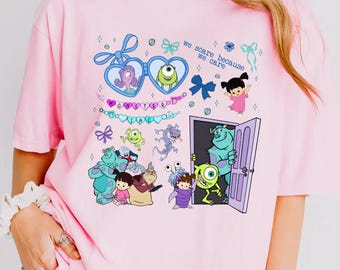 May include: Pink t-shirt with a graphic print of characters from the movie Monsters Inc. The graphic includes the text "We scare because we care".