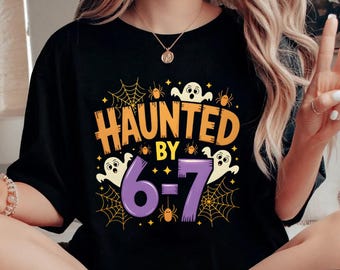 May include: Black t-shirt with the text "HAUNTED BY 6-7" in orange, white, and purple. The design includes spiderwebs, ghosts, and spiders. The shirt is part of a Halloween-themed collection.