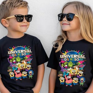 May include: Two black short-sleeve t-shirts featuring a colorful graphic print of Universal Kids Resort with various animated characters including Shrek, SpongeBob SquarePants, and Minions. The design includes bright paint splatters and text.