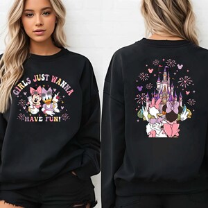 May include: Black sweatshirt featuring Minnie Mouse and Daisy Duck with the text "GIRLS JUST WANNA HAVE FUN!" on the front. The back of the sweatshirt shows a castle with fireworks and the two characters. The sweatshirt is worn by a person.