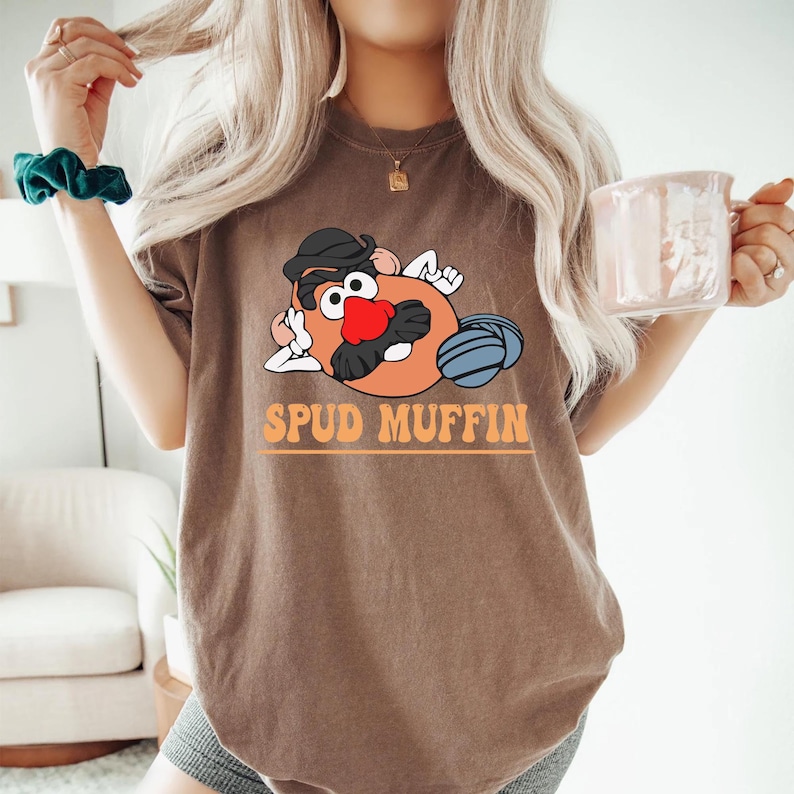 May include: A brown t-shirt with a cartoon image of Mr. Potato Head with the text "Spud Muffin" printed on the front.