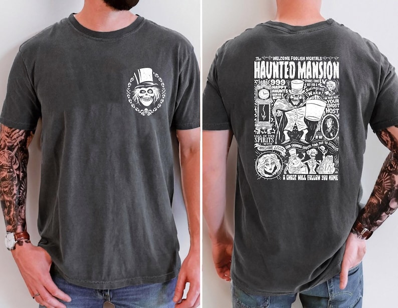 May include: A black t-shirt with a white graphic print of the Haunted Mansion attraction at Disneyland. The front of the shirt features a ghost with a top hat and the back of the shirt features a collage of characters and text from the attraction. The text on the back of the shirt reads "Welcome Foolish Mortals, The Haunted Mansion, 999 Happy Haunts, Your Ghost Host, Ghost Will Follow You Home."