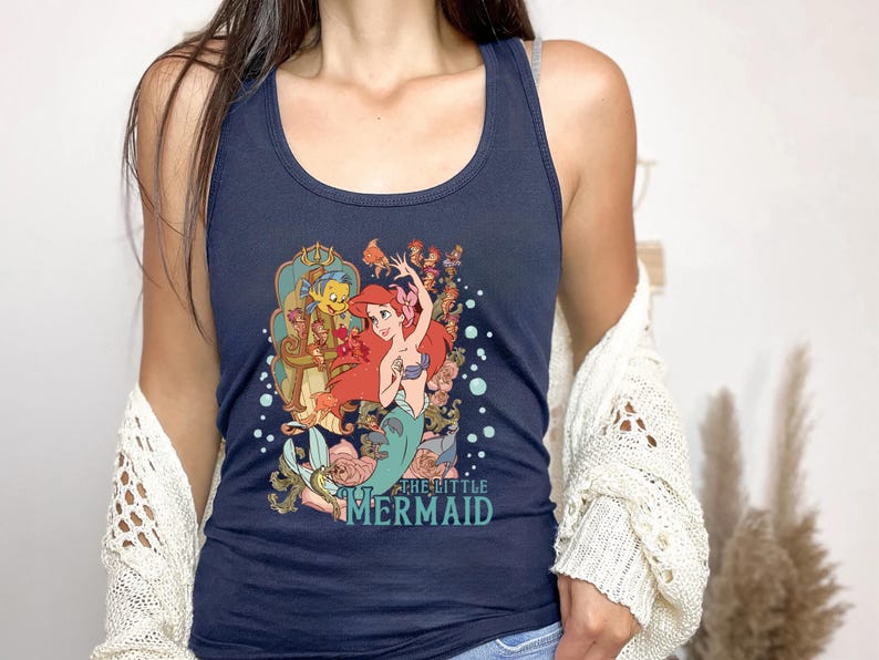 May include: A navy blue tank top with a graphic of Ariel from The Little Mermaid. The graphic features Ariel swimming with Flounder and Sebastian. The text "The Little Mermaid" is printed below the graphic.