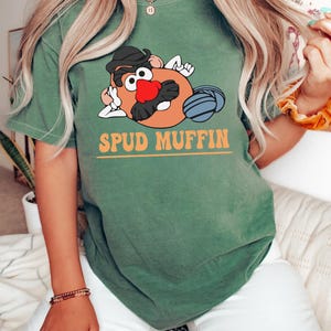 May include: A green t-shirt with a cartoon image of Mr. Potato Head with a mustache and the text "SPUD MUFFIN" in orange letters.