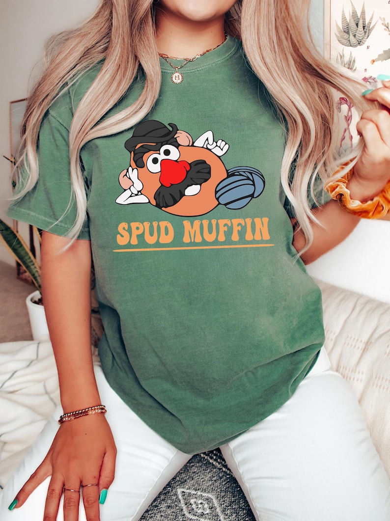 May include: A green t-shirt with a cartoon image of Mr. Potato Head with a mustache and the text "SPUD MUFFIN" in orange letters.