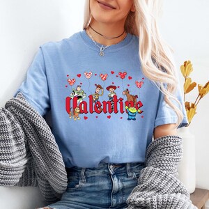 May include: Light blue t-shirt with a graphic of Toy Story characters holding heart-shaped balloons and the word "Valentine".