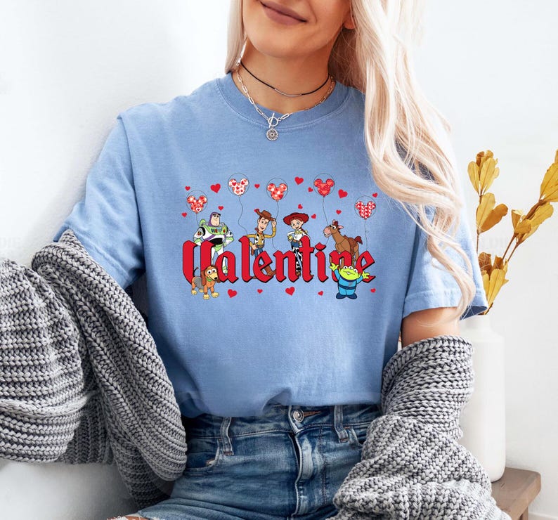 May include: Light blue t-shirt with a graphic of Toy Story characters holding heart-shaped balloons and the word "Valentine".