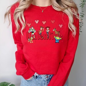 May include: Red long-sleeve sweatshirt with a graphic of Toy Story characters holding Mickey Mouse balloons and the word "Valentine" in a bold font.