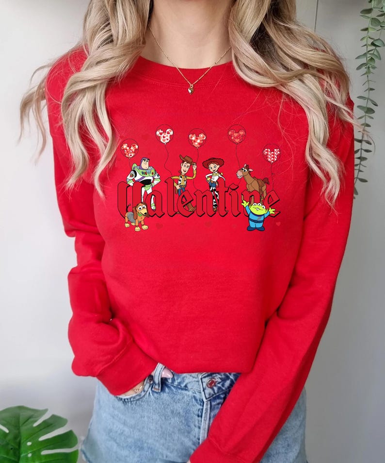 May include: Red long-sleeve sweatshirt with a graphic of Toy Story characters holding Mickey Mouse balloons and the word "Valentine" in a bold font.