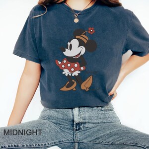 May include: A navy blue t-shirt with a vintage-style image of Minnie Mouse wearing a red polka dot dress and a flower on her head. The text "Disney" is visible below the image.