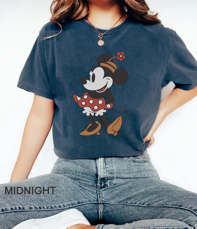 May include: A navy blue t-shirt with a vintage-style image of Minnie Mouse wearing a red polka dot dress and a flower on her head. The text "Disney" is visible below the image.