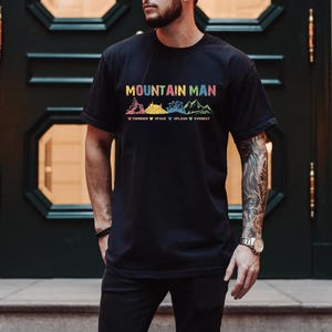 May include: A black t-shirt with the text "Mountain Man" and a graphic of mountains with the words "Timber", "Space", "Splash", and "Everest" underneath.