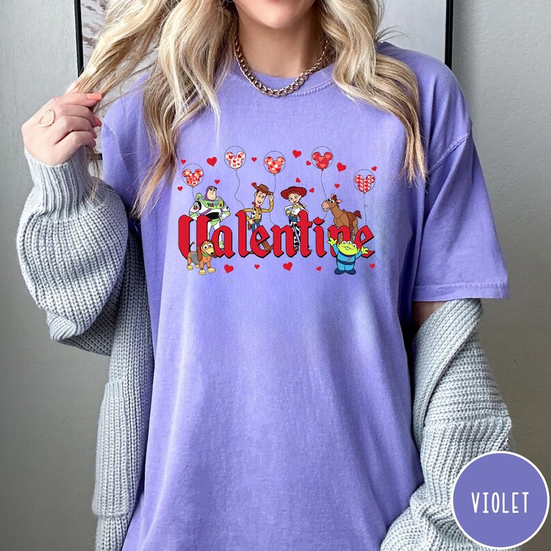 May include: Purple t-shirt with a graphic of Toy Story characters holding red heart balloons and the word "Valentine".