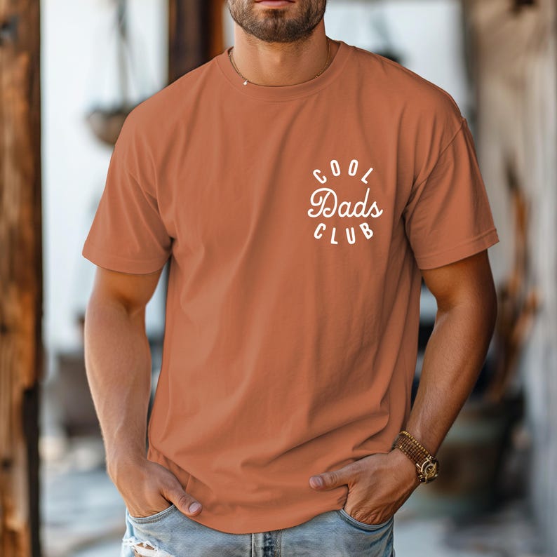 May include: A rust-colored t-shirt with short sleeves and a white circle graphic that says "Cool Dads Club".