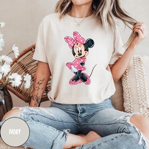 May include: A white t-shirt featuring a pink and white Minnie Mouse graphic. The shirt is ivory in colour.
