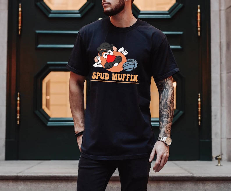 May include: A black t-shirt with a cartoon image of Mr. Potato Head wearing a baseball cap and holding a baseball bat. The text "SPUD MUFFIN" is printed in orange below the image.