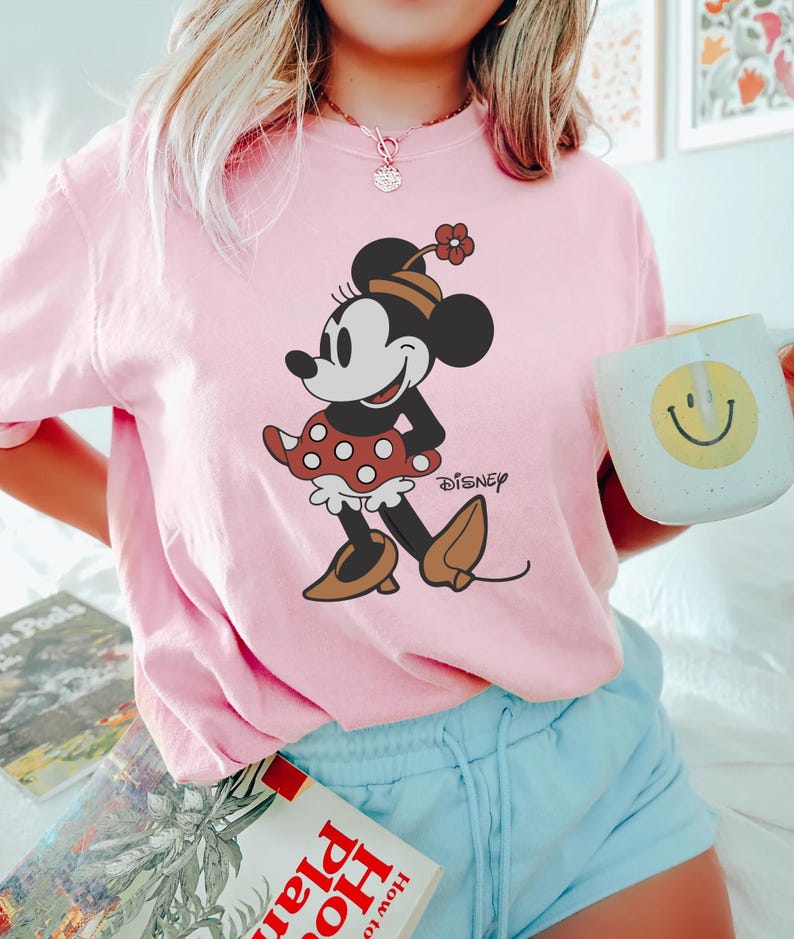 May include: Pink t-shirt with a vintage cartoon image of Minnie Mouse wearing a red polka dot dress and the word "DISNEY" printed on the bottom right corner.