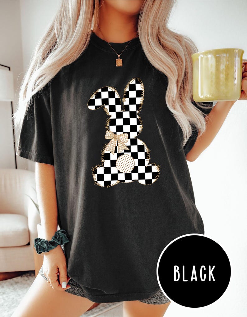 Op de afbeelding: Zwart T-shirt met een geruite konijnenprint. Het konijn heeft een gouden strik en is omrand met goud. De tekst "BLACK" is zichtbaar in de rechterbenedenhoek van de afbeelding.