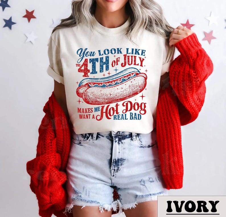 May include: A white t-shirt with a red, white, and blue graphic that says "You look like the 4th of July. Makes me want a Hot Dog real bad." The graphic features a hot dog with mustard and ketchup.