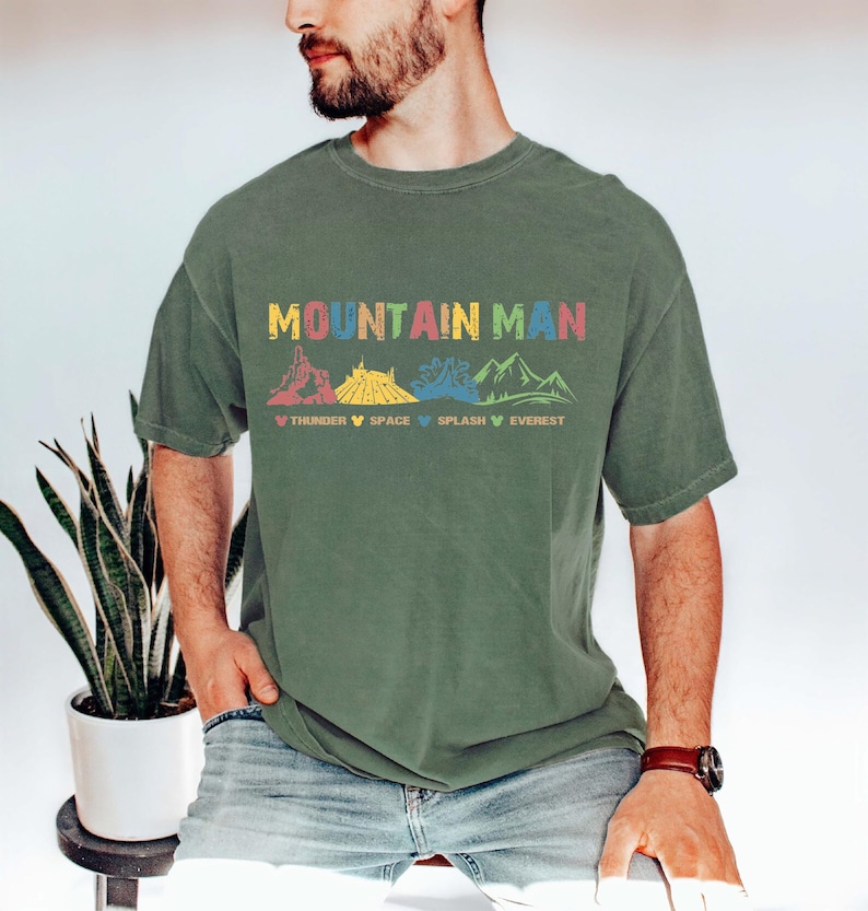May include: A green t-shirt with the text "Mountain Man" in colorful letters. The design features a row of mountains with the names "Thunder", "Space", "Splash", and "Everest" underneath.