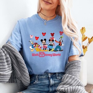 K&ouml;nnte beinhalten: Hellblaues T-Shirt mit einem Aufdruck von Mickey Mouse, Minnie Mouse, Donald Duck, Goofy und Pluto mit Herzen und dem Text "Walt Disney World".