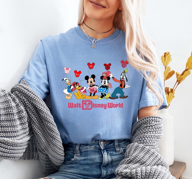 K&ouml;nnte beinhalten: Hellblaues T-Shirt mit einem Aufdruck von Mickey Mouse, Minnie Mouse, Donald Duck, Goofy und Pluto mit Herzen und dem Text "Walt Disney World".