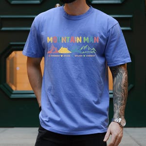 May include: A blue t-shirt with the text "Mountain Man" printed on the front. The text is surrounded by colorful illustrations of mountains with the names "Thunder", "Space", "Splash", and "Everest" printed below.