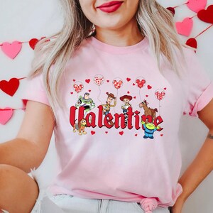 May include: Pink t-shirt with a graphic of Toy Story characters holding heart-shaped balloons and the word "Valentine".