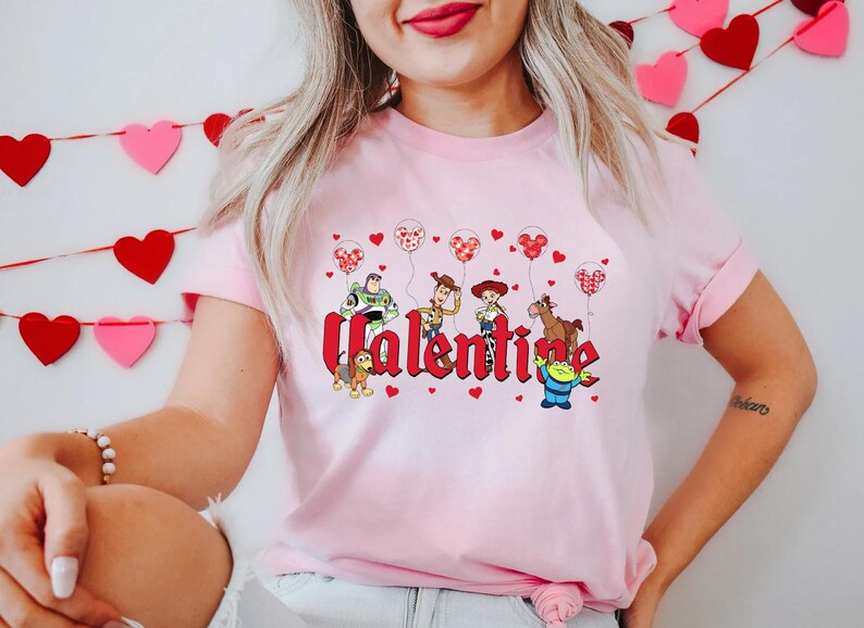 May include: Pink t-shirt with a graphic of Toy Story characters holding heart-shaped balloons and the word "Valentine".