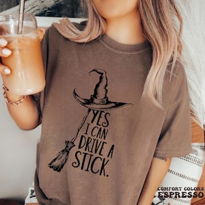 Pu&ograve; includere: T-shirt color espresso con cappello da strega nero, scopa e la scritta "YES I CAN DRIVE A STICK." La maglietta &egrave; realizzata in materiale Comfort Colors.