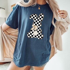Op de afbeelding: Een marineblauw t-shirt met een geruite konijnenprint. Het konijn heeft een gouden strik en is omrand met gouden draad.