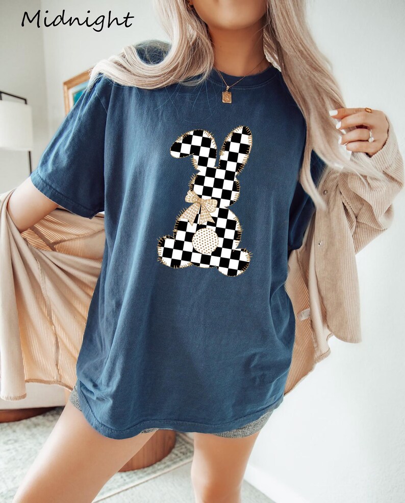 Op de afbeelding: Een marineblauw t-shirt met een geruite konijnenprint. Het konijn heeft een gouden strik en is omrand met gouden draad.