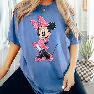 May include: An oversized blue t-shirt featuring a cartoon image of Minnie Mouse wearing a pink polka dot dress and a pink bow.