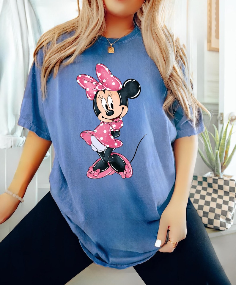 May include: An oversized blue t-shirt featuring a cartoon image of Minnie Mouse wearing a pink polka dot dress and a pink bow.