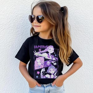 Peut inclure: Un t-shirt noir avec un motif graphique avec le mot "HUNTRA" et trois personnages de style anime en violet et blanc. La fille sur l'image porte des lunettes de soleil en forme de c&oelig;ur et un jean bleu.