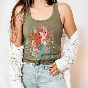 May include: A green tank top with a graphic print of Ariel, the Little Mermaid, and Flounder from the Disney movie. The text "The Little Mermaid" is printed on the bottom of the shirt.