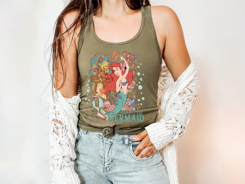 May include: A green tank top with a graphic print of Ariel, the Little Mermaid, and Flounder from the Disney movie. The text "The Little Mermaid" is printed on the bottom of the shirt.