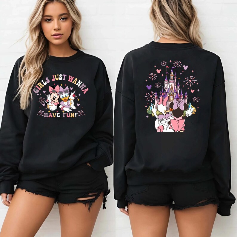 May include: Black sweatshirt featuring Minnie Mouse and Daisy Duck with the text "GIRLS JUST WANNA HAVE FUN!" on the front. The back of the sweatshirt shows a castle with fireworks and the two characters. The sweatshirt is worn by a person.