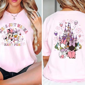 May include: Pink t-shirt featuring Minnie Mouse and Daisy Duck with the text "GIRLS JUST WANNA HAVE FUN!" on the front. The back of the shirt shows a castle and the same characters. The design includes fireworks and balloons.